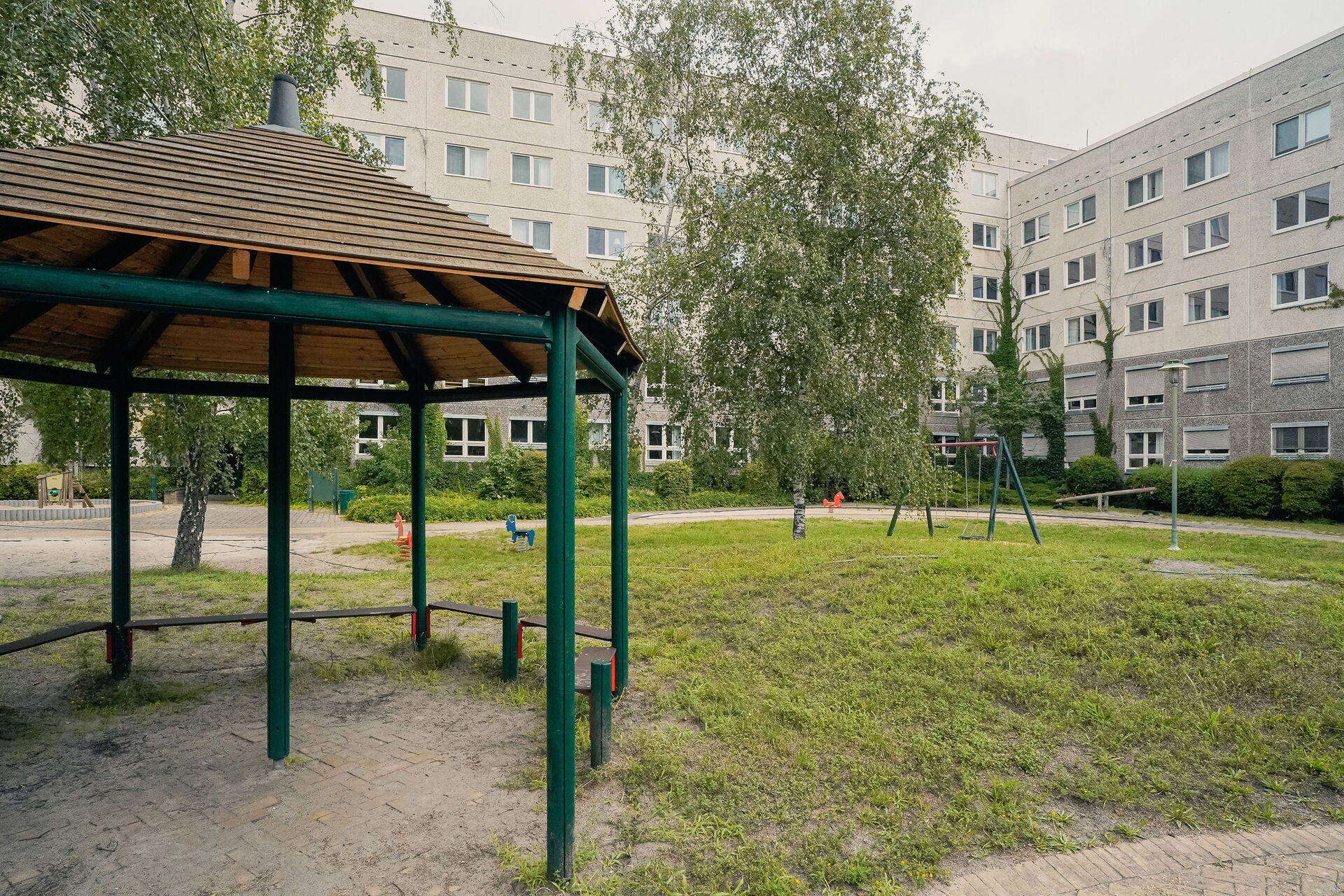 Draußen. Spielplatz, Schaukel, Wippe. Umrahmt von einem Gebäudekomplex.