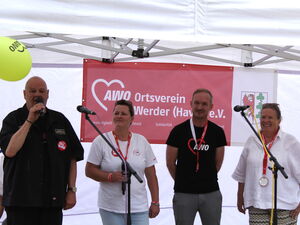 2 Frauen in weißen T-Shirts, 2 Männer in schwarzen T-Shirts. Mikrone stehen vor ihnen. Mann links außen hält ein Mikro und spricht.