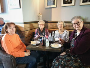 4 Frauen sitzen bei Getränken und Kuchen an einem kleinen 4-eckigen Tisch in einer Nische.