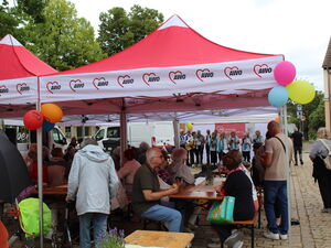 Rote AWO Pavillons mit Biertischgarnituren. Menschen die essen und trinken. Im Hintergrund der Chor.