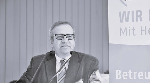 Schwarz-Weiß Foto: Mann mit Brille, Anzug, weißem Hemd in Krawatte an einem Rednerpult bei der AWO.