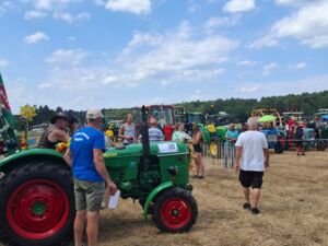 Viele Trecker auf einer trockenen Wiese. Schaulustige die sich umsehen. Alle tragen sommerliche Kleidung.