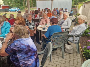 Viele ältere Menschen auf Gartenstühlen und Kaffeetafeln.