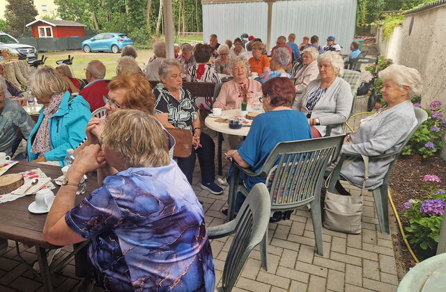 Viele ältere Menschen auf Gartenstühlen und Kaffeetafeln.