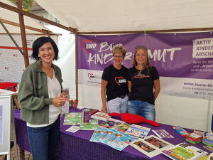 Stand von AWO Büro Kindermut. Zwei Frauen im Stand mit viel Info-Material. Davor lächelt Frau Aubel in die Kamera.