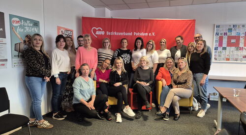 Gruppenbild: In einem Konferenzraum vor einer roten AWO Stoffwand stehen und sitzen 20 Menschen.