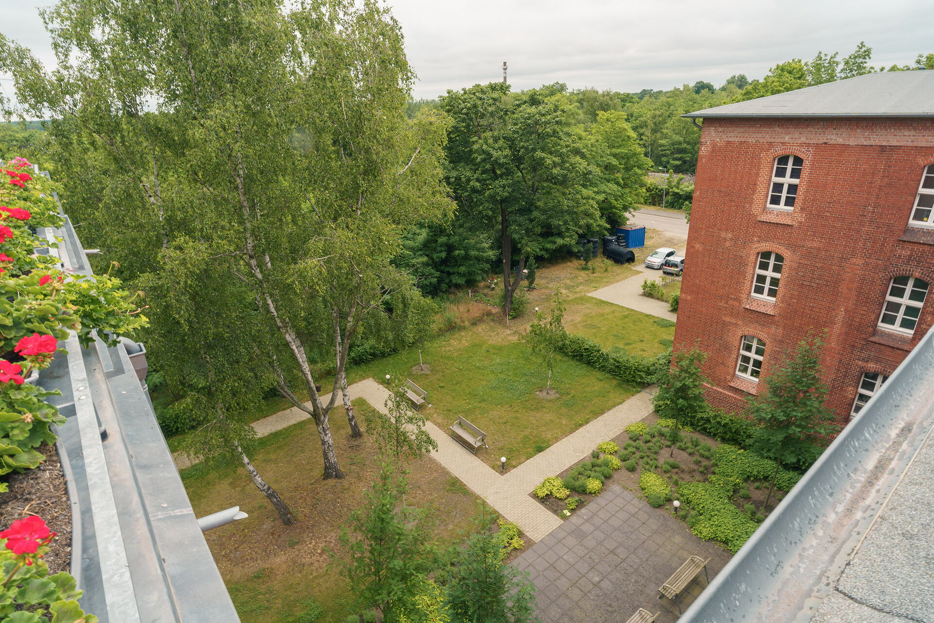 Blick von der Dachterrasse nach unten. Bäume, Wiese, Bänke, kleiner Garten.
