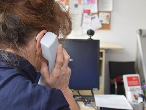 Frau von hinten an einem Schreibtisch sitzend mit Telefonhörer am Ohr.