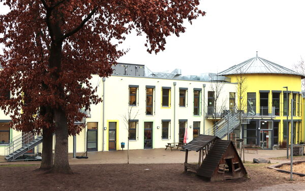 Gebäude von außen, zwei Geschosse. Schule und Hort. Außentreppen führen zum zweiten Stockwerk, Fassade ist gelb.