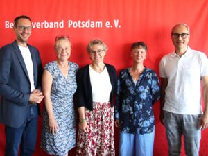 Gruppenbild, 5 Personen vor roter AWO Wand mit AWO Logo. 3 Frauen eingerahmt von zwei Männern. Alle sehen freundlich lächelnd in die Kamera.