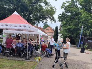 Gute Laune, Stimmung. Ein Mann mit Mikro singt. Alte Menschen, tanzen, klatschen und feiern fröhlich. Das Wetter ist sonnig. Unter einem AWO Pavillon sitzen frohe Menschen im Rollstuhl, auf dem Rollator und auf Stühlen.