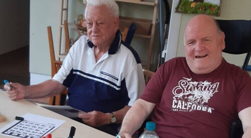 2 Männer sitzen am Tisch und spielen Bingo.