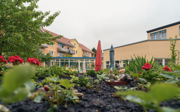 Hier sehen sie kleine Tonfiguren in einem Beet vor einem Seniorenzentrum
