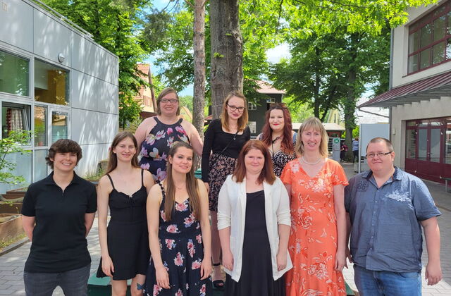 Gruppenbild. 9 Menschen stehen unter einem Baum und lächeln fröhlich in die Kamera.