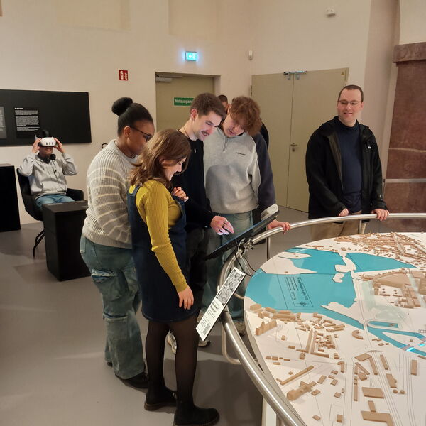 4 junge Menschen stehen im Museum an einem Monitor der bei einem großen, dreidimensionalen Brandenburg-Relief im Museum, das die topografische Landschaft mit Hügeln und Seen zeigt.