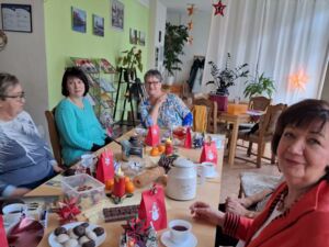 Gedeckter Kaffeetisch mit kleinen Weihnachtstüten und Süßigkeiten. Vier Frauen sitzen an dem Tisch.