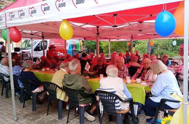 Pavillons mit Luftballons geschmückt. Menschen sitzen bei Kaffee und Kuchen darunter an langen Tischen.