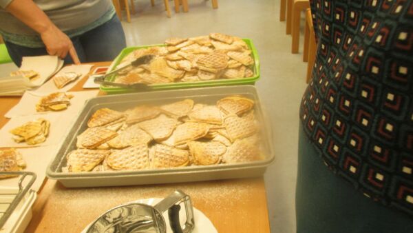 Viele Herz-Waffeln mit Puderzucker in zwei Blechen der Puderzuckerstreuer steht daneben.