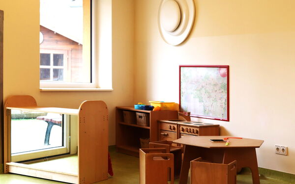 Heller Raum, in der Ecke eine kleine Spiel-Küche mit Spühle, Herd, Tisch und Stühlen aus dunklem Holz für kleine Kinder.