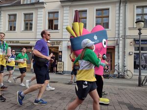 Ein pinkes Herz Maskottchen rennt mit anderen Teilnehmen an der Kamera vorbei.