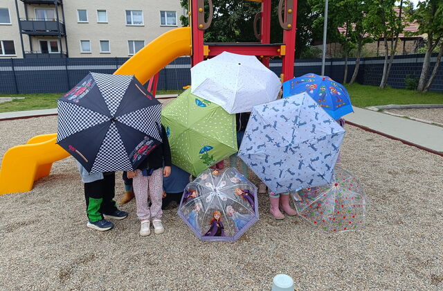 Kinder auf einen Spielplatz vor einer Rutsche. Viele bunte Regenschirme verdecken die Kinder.