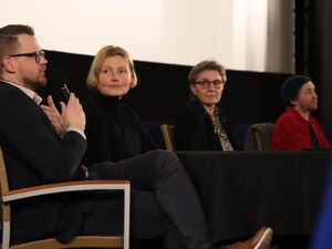2 Männer, zwei Frauen sitzen auf dem Podium im Kinosaal. Ein Mann ganz links spricht in das Mikrofon.