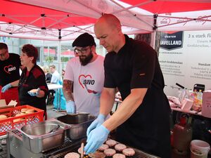 Grill- und Burgerstand. Eine Frau und 3 Männer in der Bedienung und Zubereitung. Ein Mann wendet die Patties. Eine Frau belegt Burger.