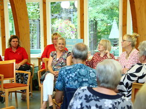 Großer Raum mit großen Fensterfronten. In dem Raum sitzen Menschen. Größtenteils Frauen.