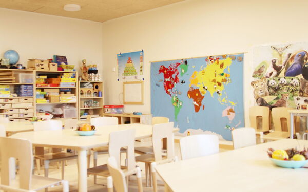 Raum mit Tischen und Stühlen und Regalen. In den Regalen sind Spiele. An der Wand eine große Weltkarte.