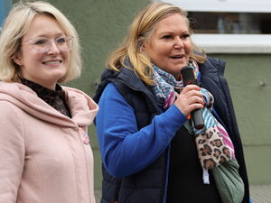 3 Frauen, in der Mitte eine Frau mit entschlossenem Gesichtsausdruck. Sie spricht in ein Mikrofon. Die Frau rechts trägt eine Trillerpfeife um den Hals.