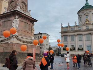 Vereinzelte Menschen auf dem alten Markt, mit orangene Luftballons, Schaals, Schuhen oder Jacken.