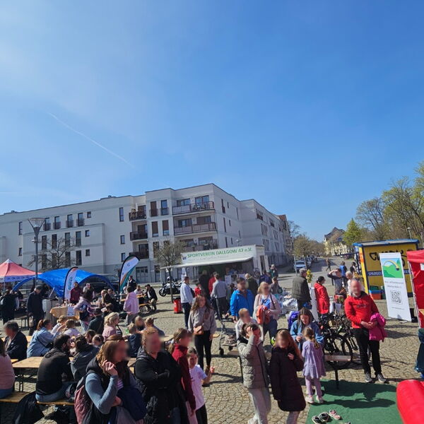 Viele Menschen auf einem großen Platz. Rechts am Bildrand eine rote Hüpfburg. Markt Atmosphäre bei blauem Himmel.