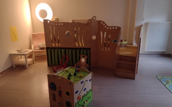 Eine Spiellandschaft aus Holz und ein großer Holzwürfel und eine separater Bereich mit Sessel und Tisch.
