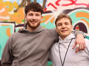 Zwei junge Männer, vor einer Graffiti-Wand. Beide lächeln in die Kamera.