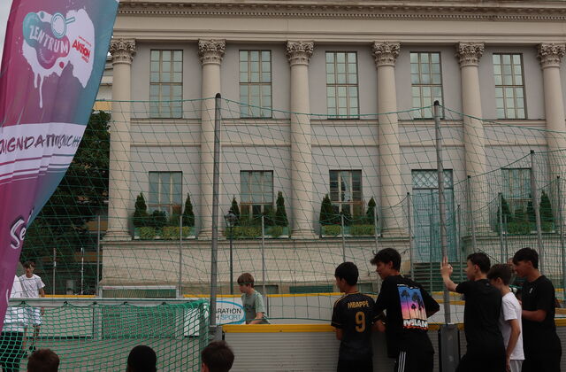 Mit Netz umrandetes kleines Fußballfeld. Jungen stehen davor. Im Hintergrund groß das Potsdam Museum.