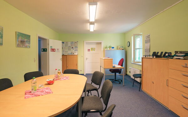 Besprechungsraum. Ovaler Tisch mit 6 Stühlen, rechts an der Wand steht ein Schrank.