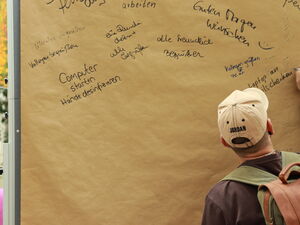 Teilnehmender schreibt etwas an ein großes Flipchart-Papier.  Da stehen schon andere Stichpunkte: "Guten Morgen wünschen", "Kollegen begrüßen", Computer starten - Hände desinfizieren"