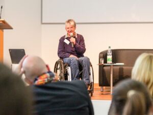 Fr. Dr. Arnade von der ISL Berlin stellt dem Fachtagspublikum neben dem Rednerpult vom Rollstuhl aus das Mentorenprojekt  Job-Win-Win vor.