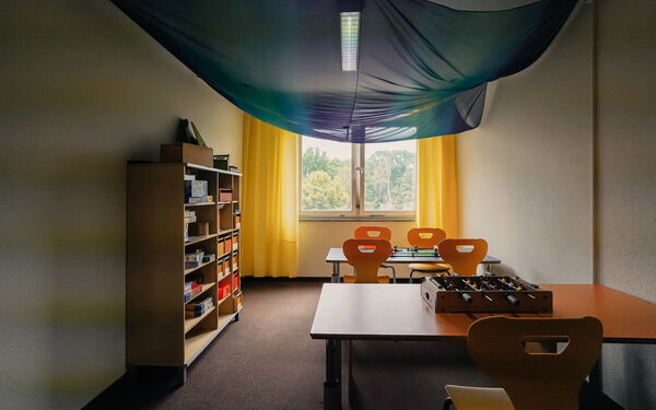 Spielzimmer, 2 Tische mit Stühlen an der Wand. Auf einem Tisch ein kleiner Tischkicker, an der linken Wand ein Regal mit Spielen.