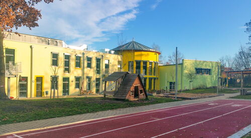 Großes gelbes Schulgebäude. Laufbahn für Sport, draußen auf dem Schulhof.