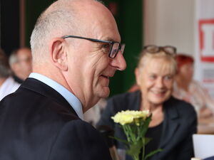Im Vordergrund ein Mann mit sehr kurzen grauen Haaren und Brille. Weitere Personen am Tisch.