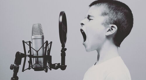 Junge schreit oder singt mit weit geöffnetem Mund in ein Studiomikrofon.