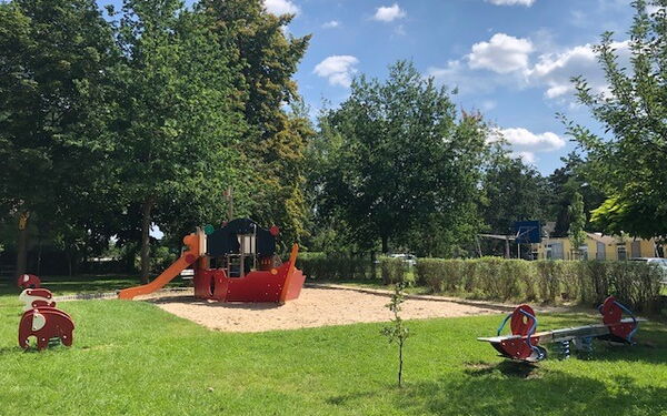 Spielplatz mit Wippe, Sandkasten und ein Klettergerüst mit Rutsche das aussieht wie ein Schiff.