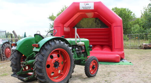 Grüner Traktor vor roter Hüpfburg.