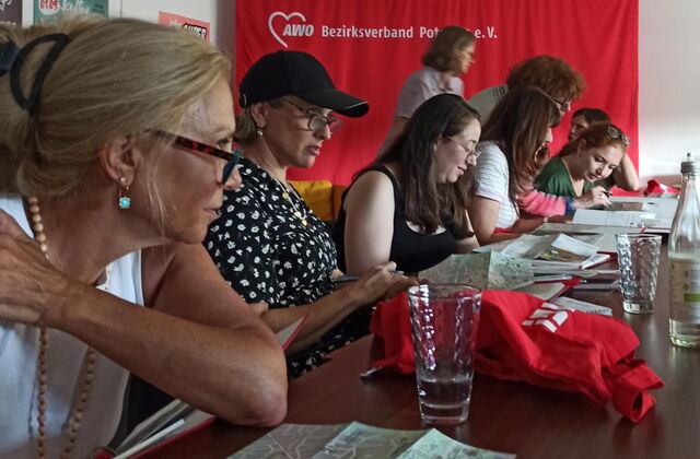 Frauen sitzen an einem Tisch. Auf dem Tisch: Gläser, Wasserflaschen, Stadtpläne.