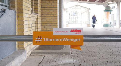 Auf einem Schild steht der Hashtag Eine Barriere weniger