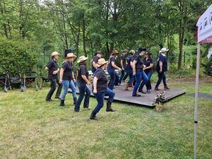Line-Dance-Gruppe. Menschen auf und neben einer kleinen Bühne im Freien mit Cowboyhüten.