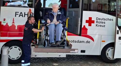 Reisebus vom Deutschen Roten Kreuz mit Hebebühne. Ein älterer Herr im Rollstuhl wird vom DRK Mitarbeiten aus Bus befördert.