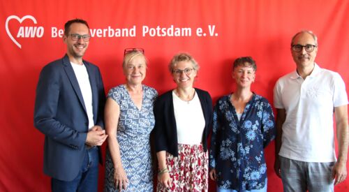 Gruppenbild, 5 Personen vor roter AWO Wand mit AWO Logo. 3 Frauen eingerahmt von zwei Männern. Alle sehen freundlich lächelnd in die Kamera.