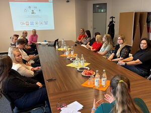 Konferenzraum. Langer Tisch mit Menschen. An der Wand eine Präsentation.